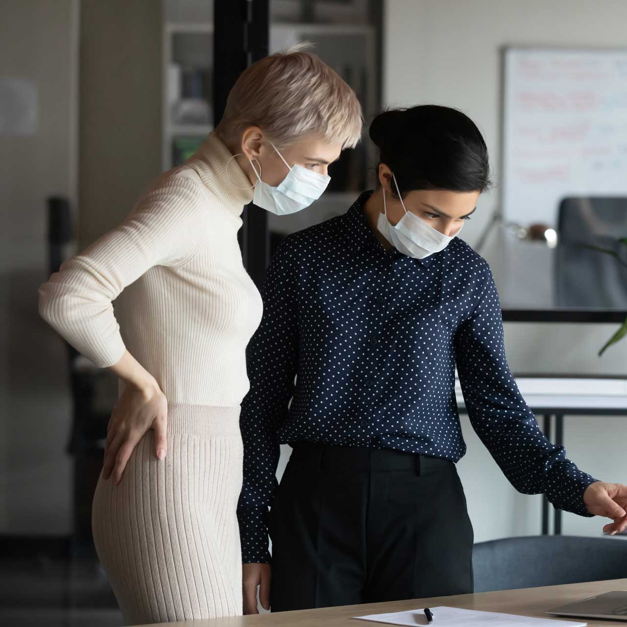Focused two women in medical protective masks working in office.